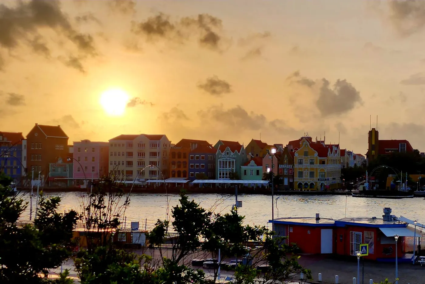 The pastel waterfront of Willemstad, Curaçao, glowing at golden hour — the whole row of Handelskade facades lit by a low sun